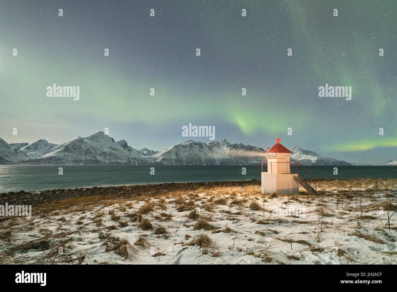 Las luces del norte y las estrellas iluminan el faro enmarcado por el mar helado, Djupvik, Lyngen Alpes, Troms, Noruega Foto de stock