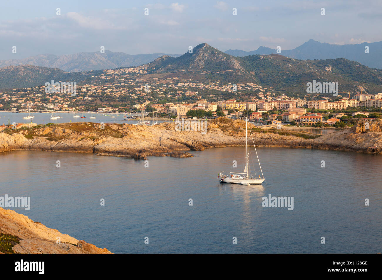 Un bote de vela en el mar claro alrededor de la aldea de Ile Rousse al atardecer, Región de Balagne, Córcega, Francia, el Mediterráneo, Europa Foto de stock