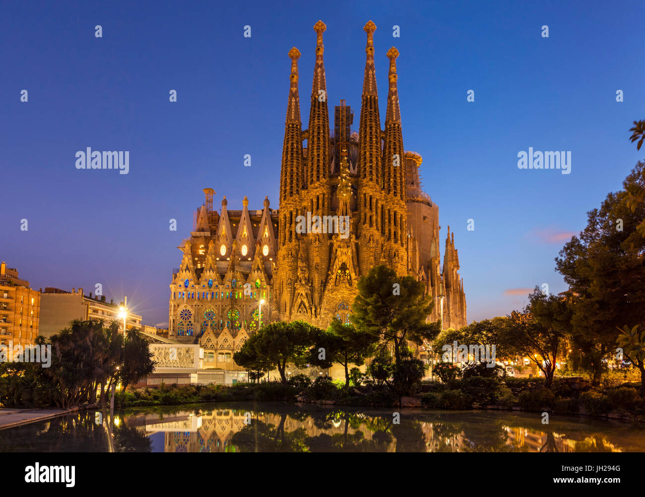La iglesia de La Sagrada Familia iluminada de noche diseñado por Antoni Gaudí, UNESCO, reflejado en la piscina, Barcelona, Cataluña, España Foto de stock