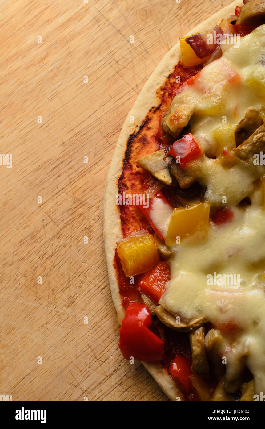 Fotografía cenital de una mezcla de vegetales pizza vegetariana coronada con queso mozzarella rayado sobre una tabla de cortar de madera antigua con espacio de copia. Foto de stock