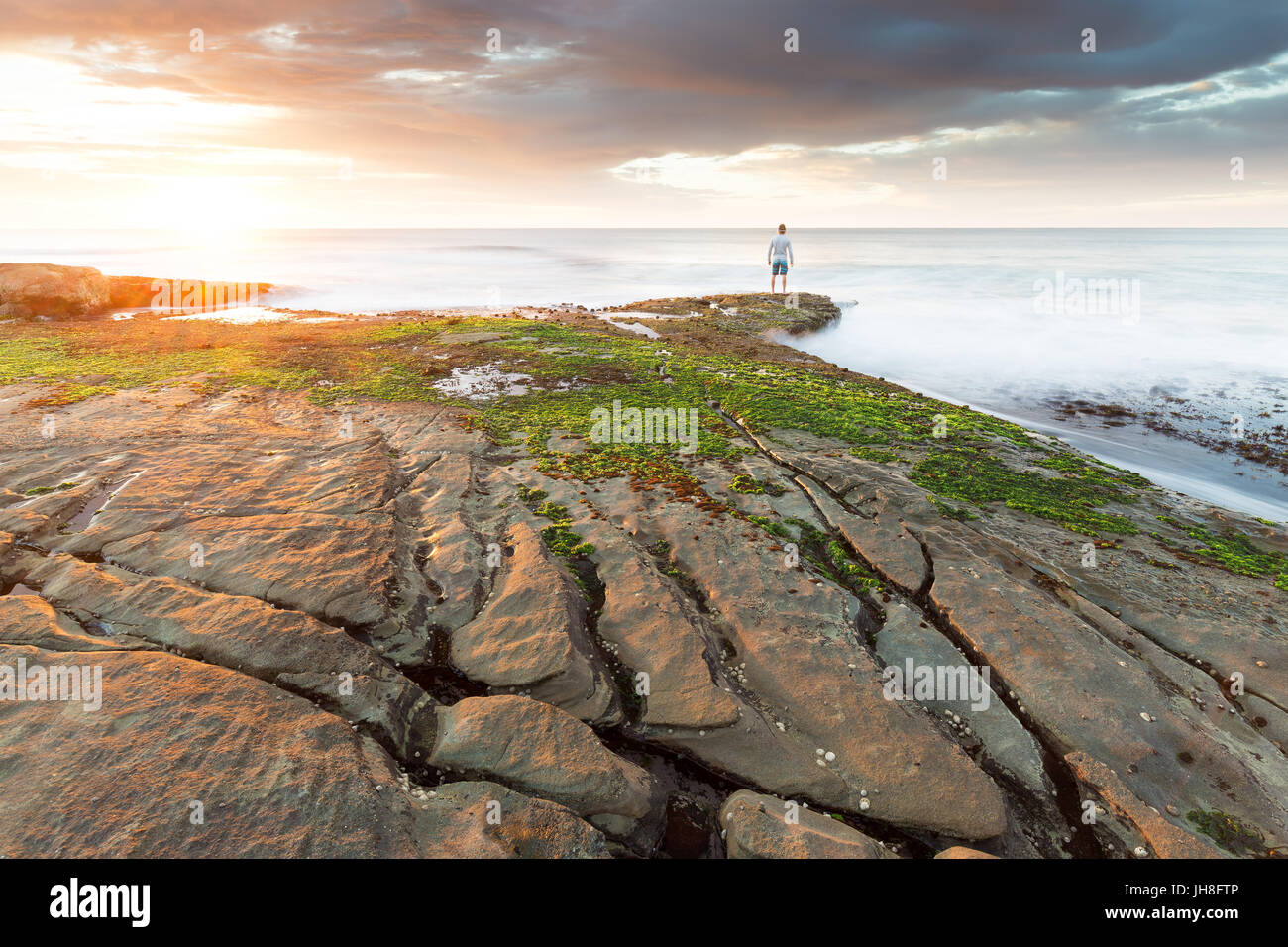 Una persona está al borde del agua y relojes un hermoso amanecer ilumina el océano y a la costa que rodea. Foto de stock