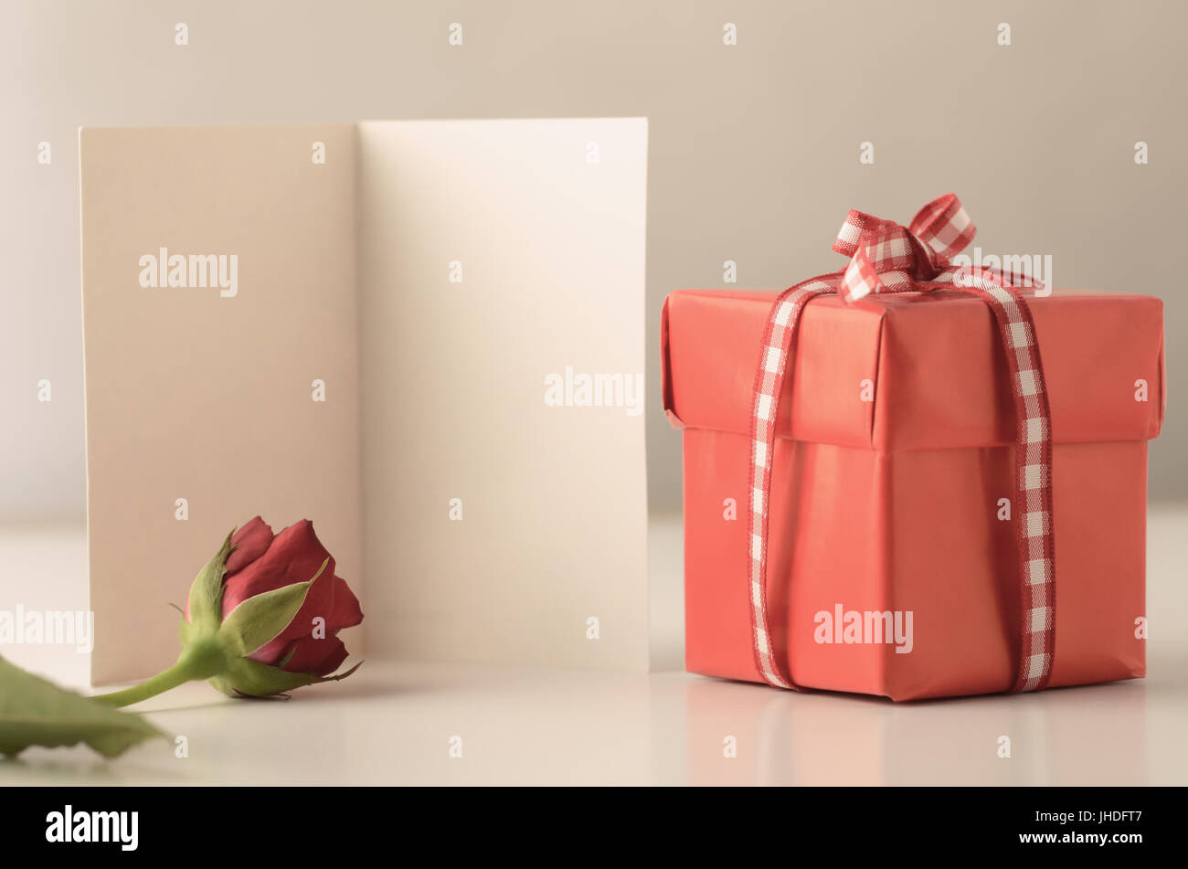 Una sola plaza pequeña caja de regalo con tapa, atado a un lazo con cinta de tela de algodón a cuadros en un cuadro blanco con una rosa y una tarjeta que proporciona copia de espacio abierto. Foto de stock