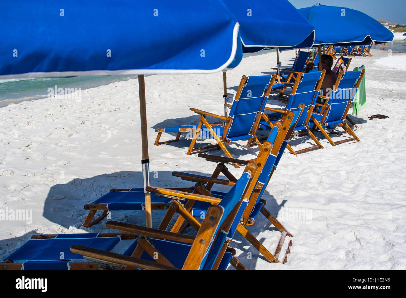 Una fila de sillas de playa y sombrillas azules que se establecieron a lo largo del agua. Foto de stock