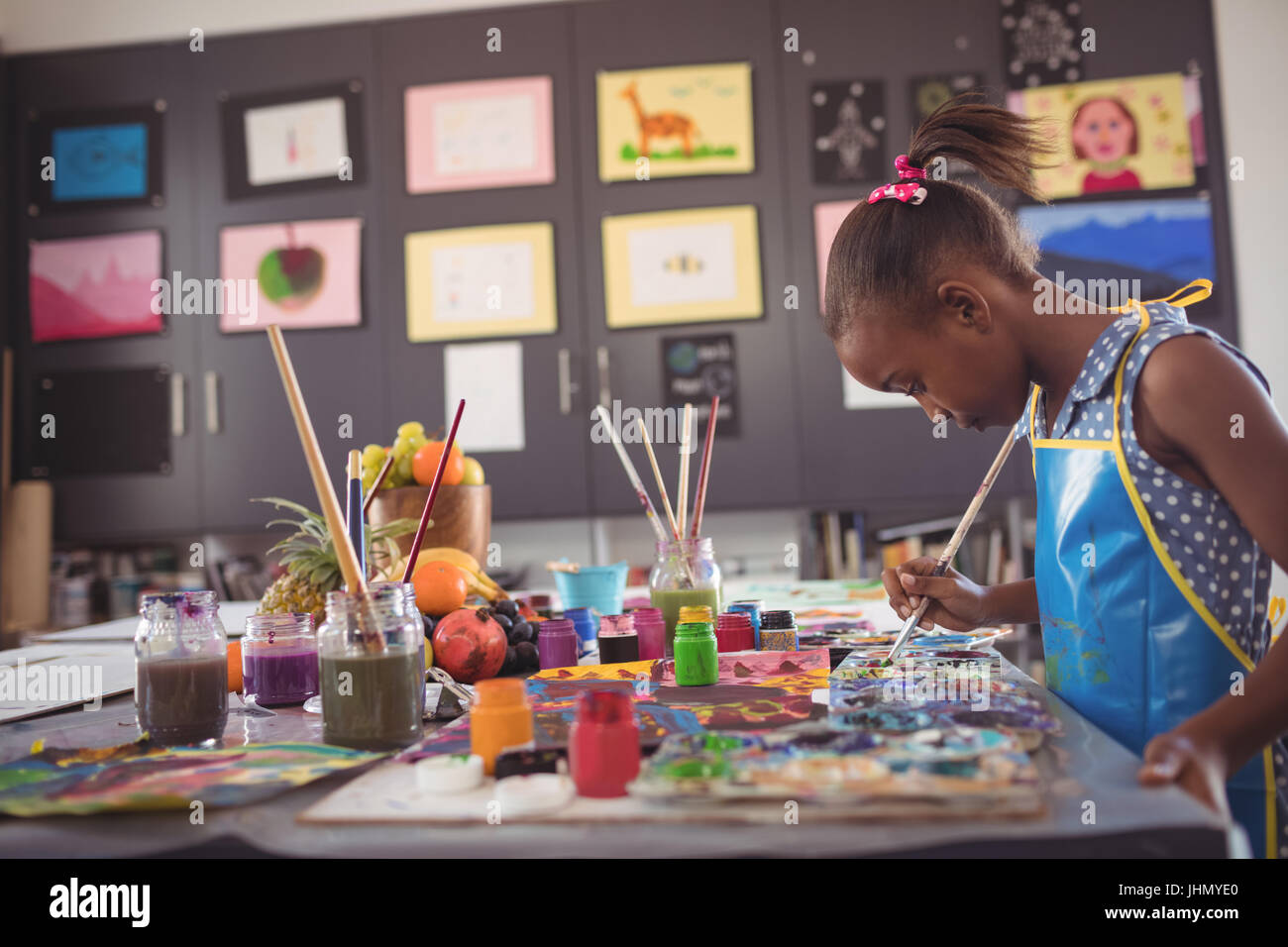 Vista lateral de la Chica sujetando el cepillo por paletas de colores en el pupitre en el aula Foto de stock