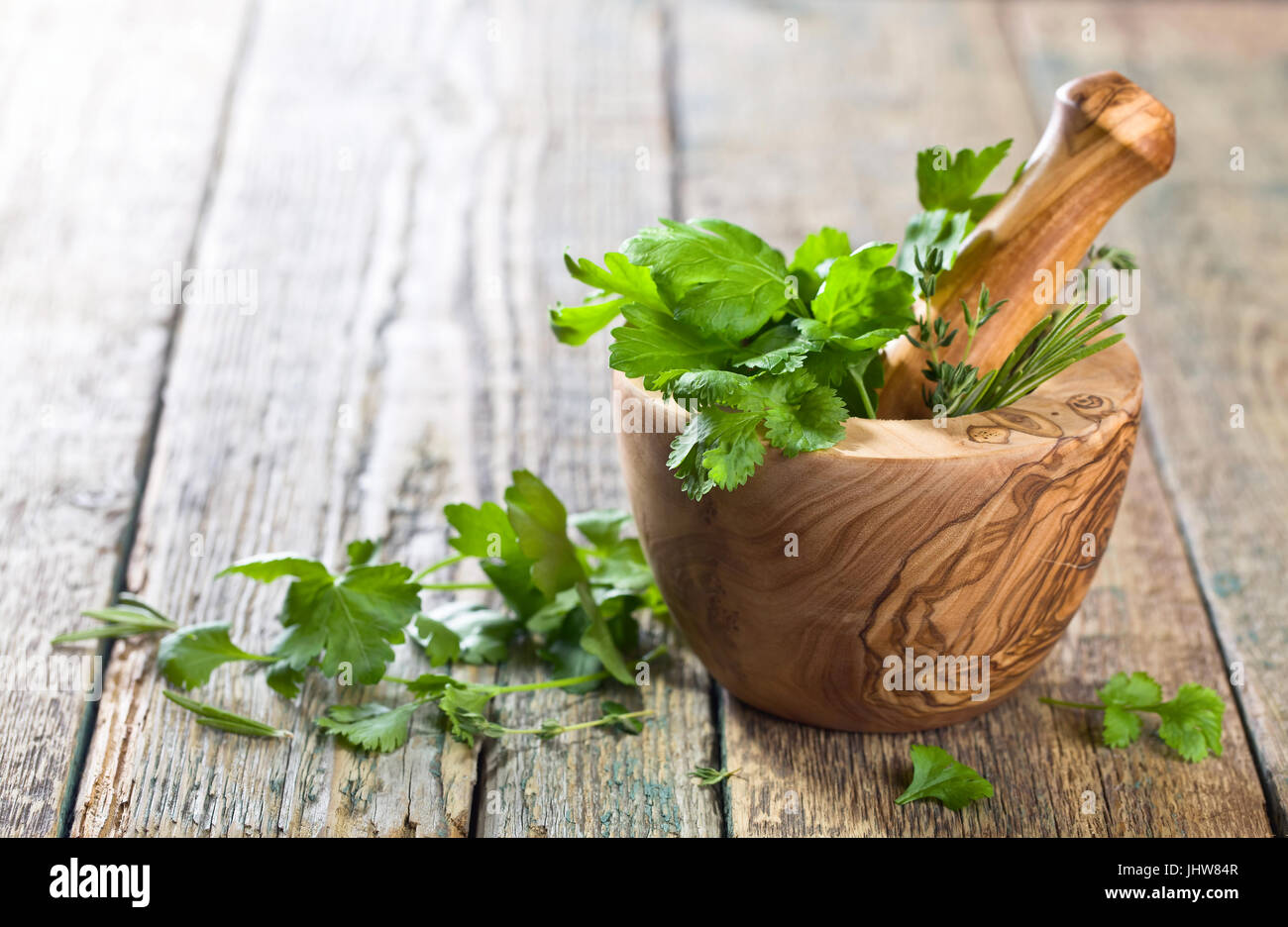 Diferentes hierbas sobre una mesa de madera antigua . Mortero de madera con el romero, el tomillo, el cilantro y el perejil. Foto de stock