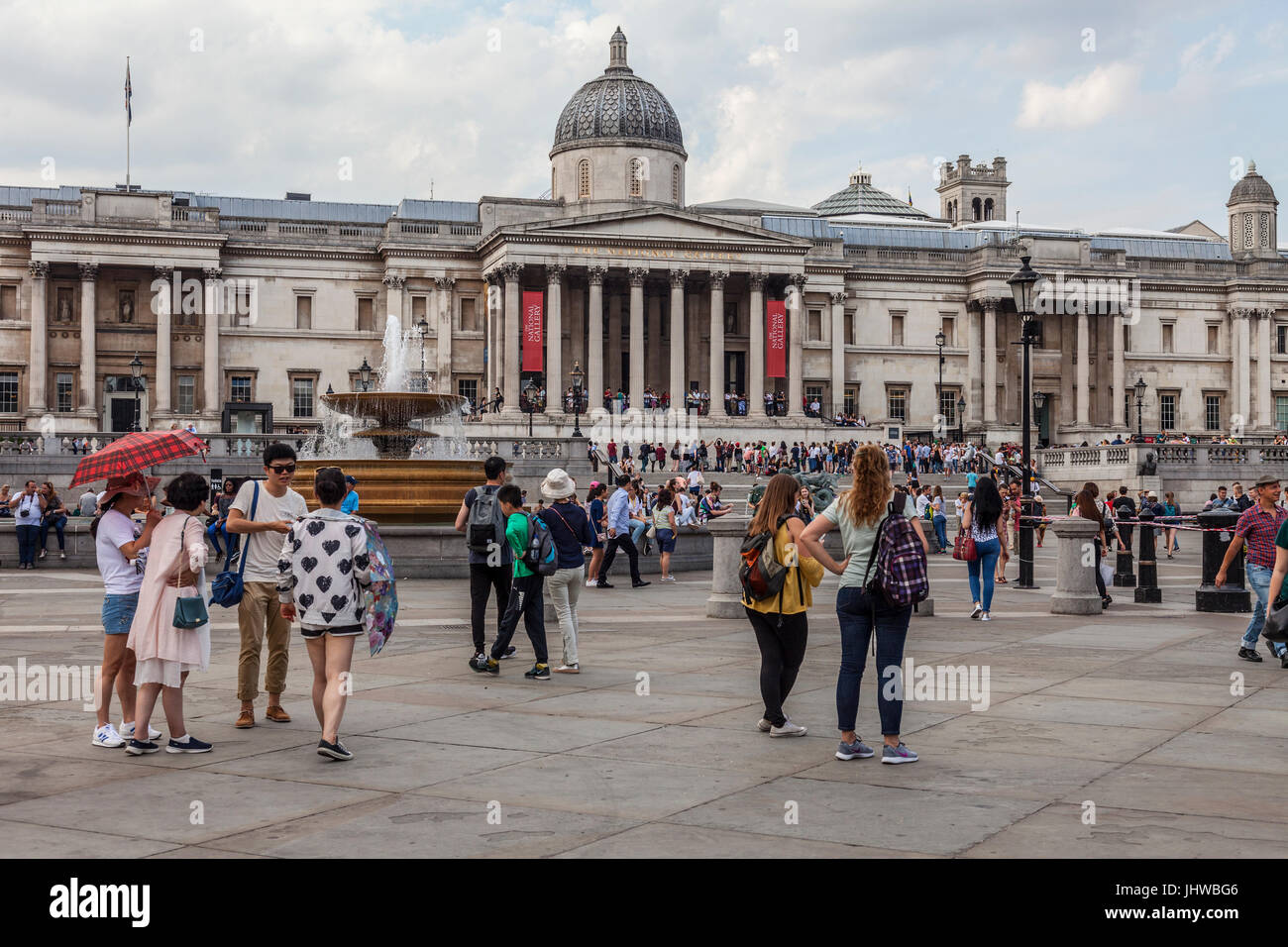 Los turistas y lugareños de pie y sentado fuera de la Galería Nacional en Trafalgar Square, Londres, relajarse, charlar, comprobación de teléfonos, teniendo photog Foto de stock