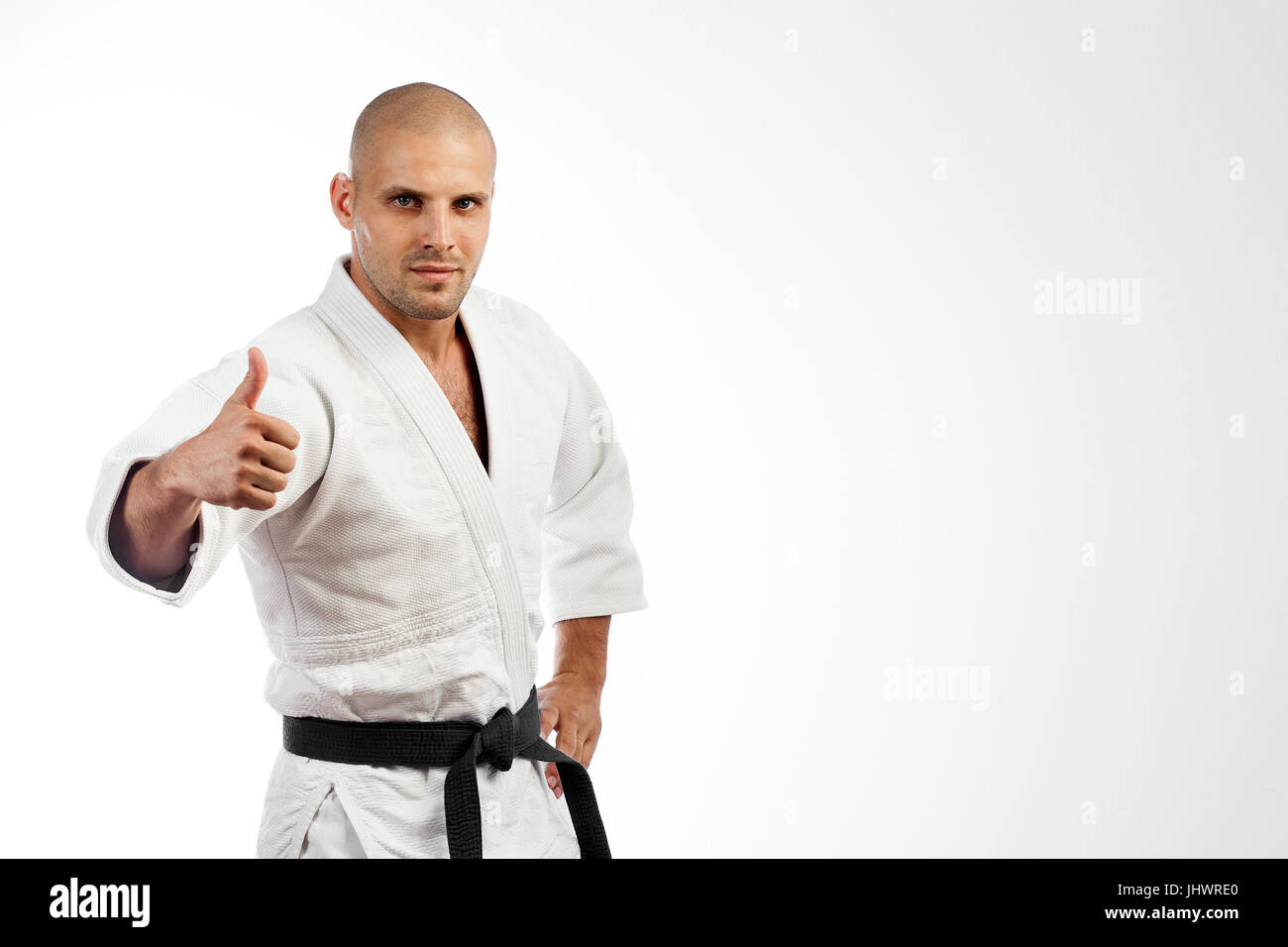 Joven luchador en un kimono blanco con cinturón negro de judo, jiu-jitsu  posando sobre fondo blanco aisladas, sosteniendo un pulgar arriba  Fotografía de stock - Alamy