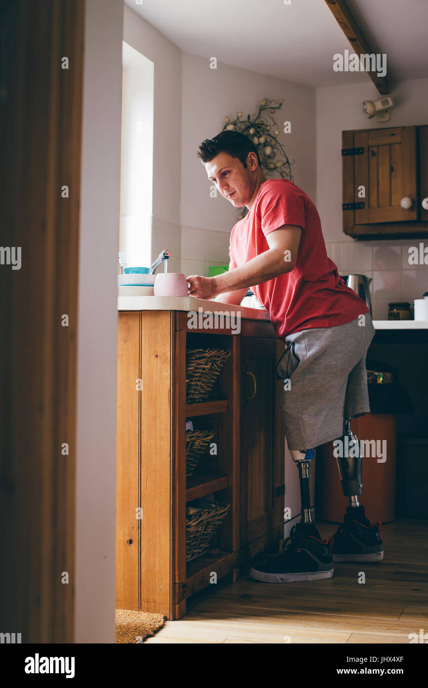 Hombre cuadriplégico lavando los platos en el fregadero de la cocina de su casa. Foto de stock