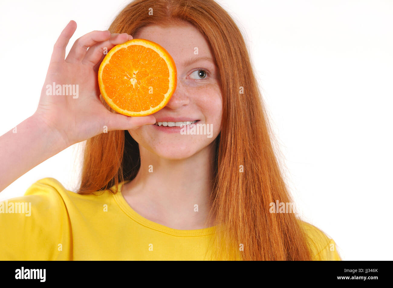 Pelo rojo adolescente Chica sujetando pedazo de naranja en frente de sus ojos mientras está de pie contra el fondo blanco. Excelente comida para un estilo de vida saludable. Natural Foto de stock