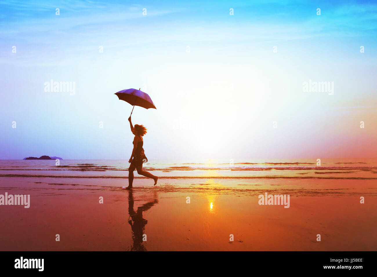 Silueta de niña despreocupada, feliz saltando con sombrilla en la playa al atardecer, libertad y alegría, concepto Foto de stock