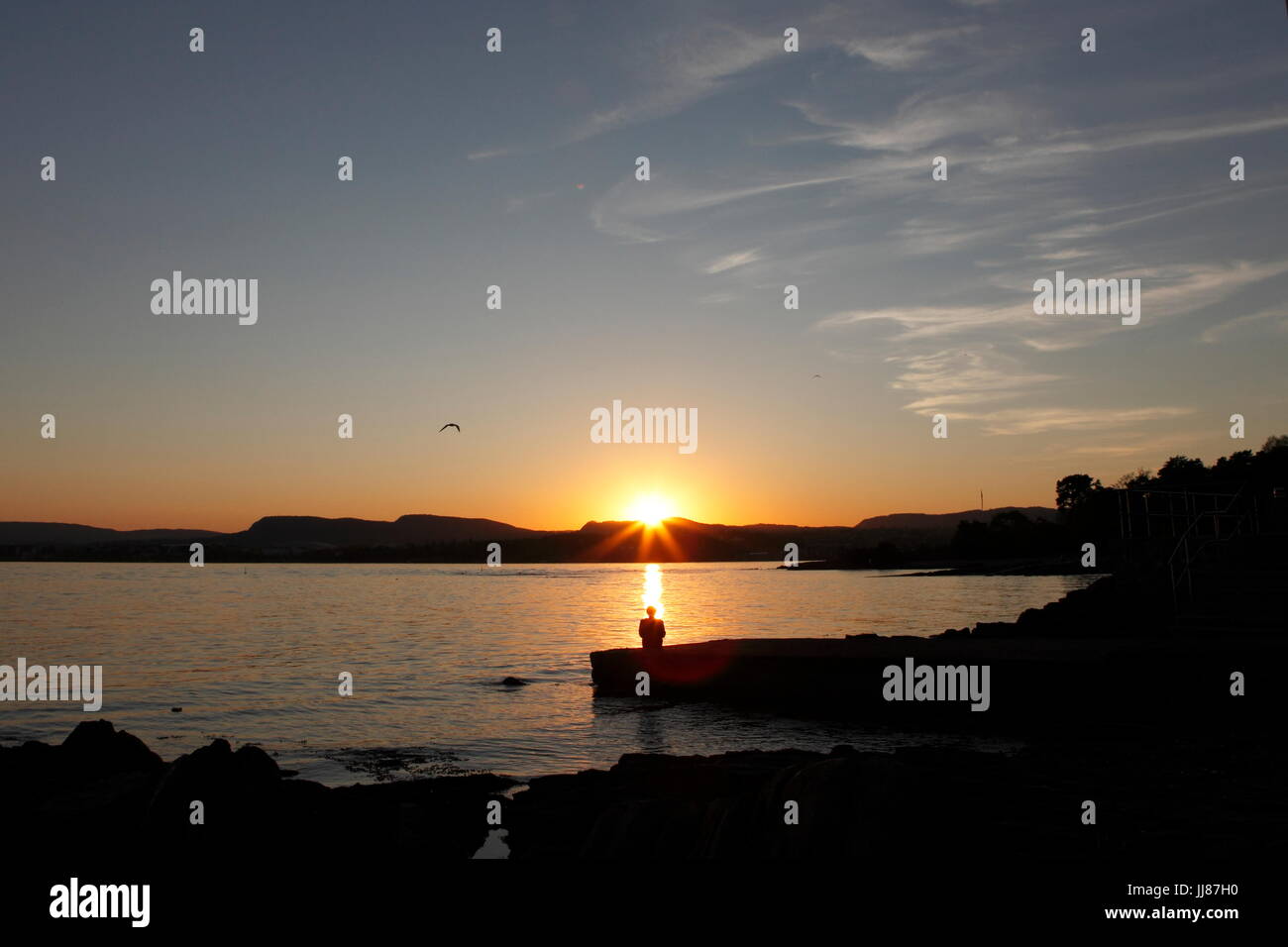 Una mujer está viendo la puesta de sol desde la playa más popular, Huk, en Oslo, Noruega. Relájese, disfrute y meditar, mindfulness Foto de stock