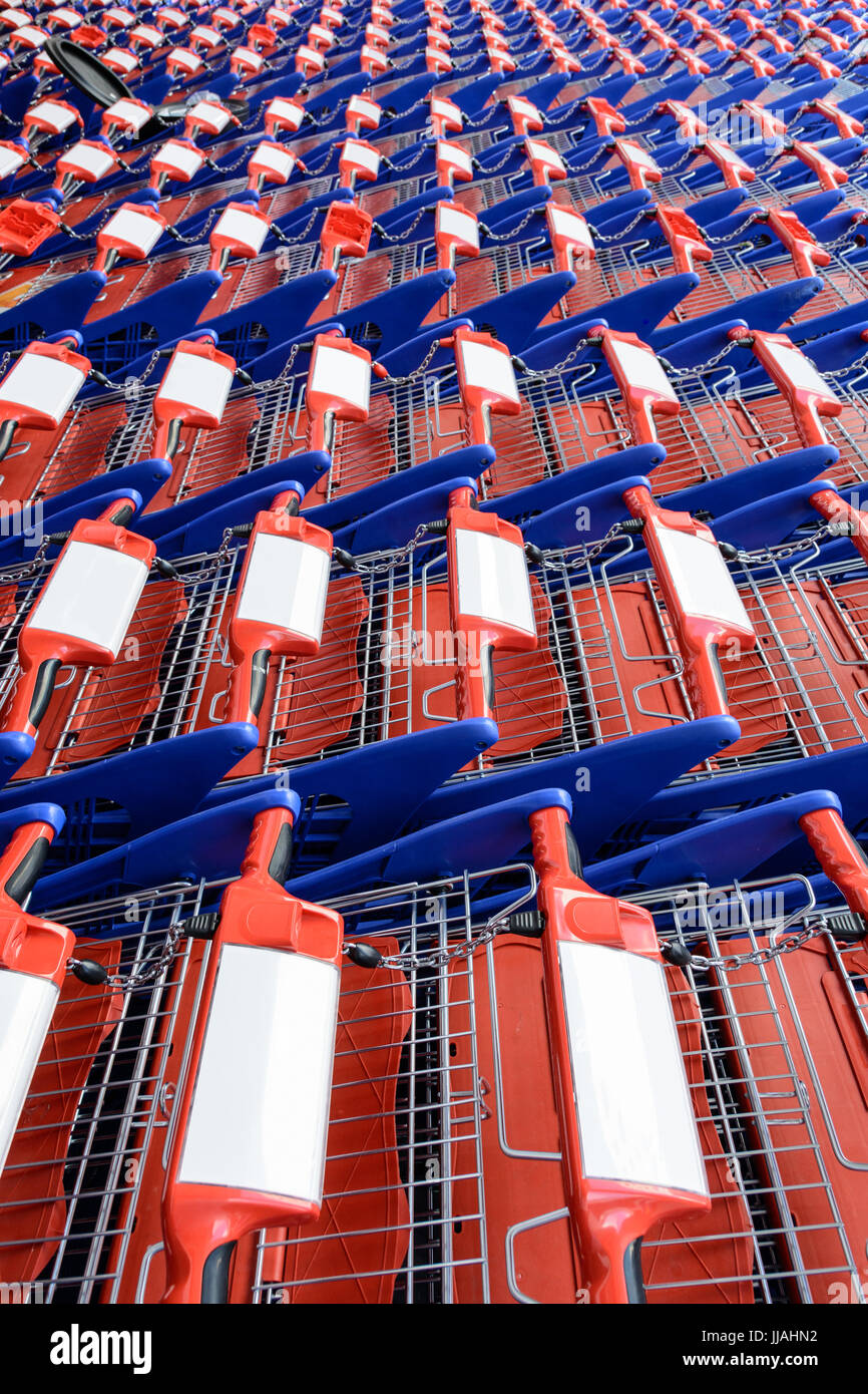 Filas de carritos de compras rojos y azules anidado entre sí en un supermercado. Foto de stock