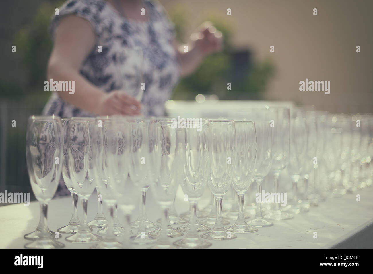 Mujer tomando un champagne desde una mesa con copas alineadas Foto de stock