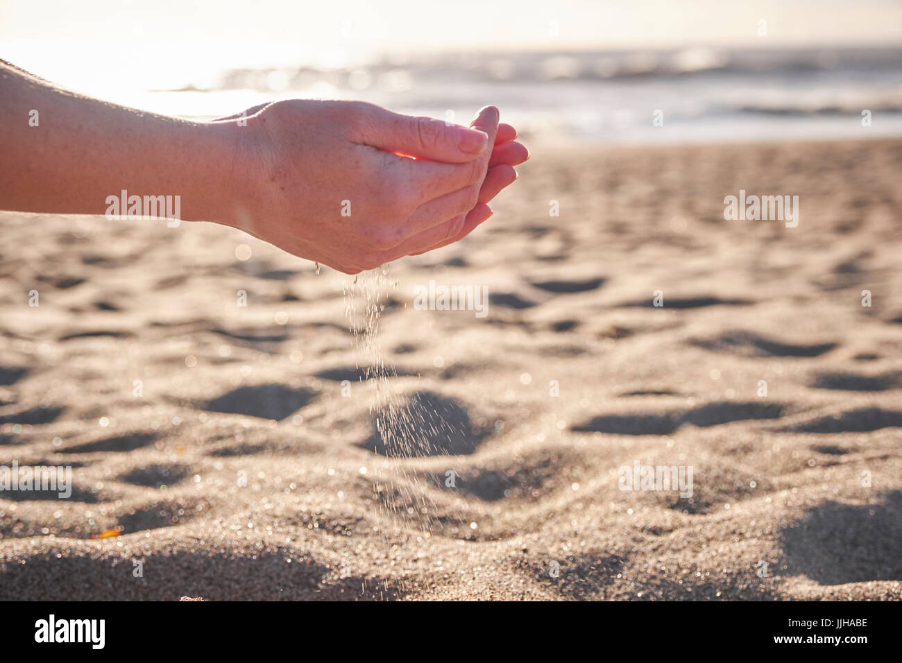 Una joven mujer de tamizar a través de sus manos de arena en la playa. Foto de stock