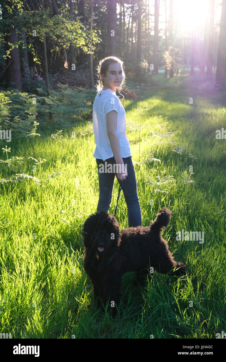Una adolescente de pie con su cachorro en un bosque iluminado. Foto de stock