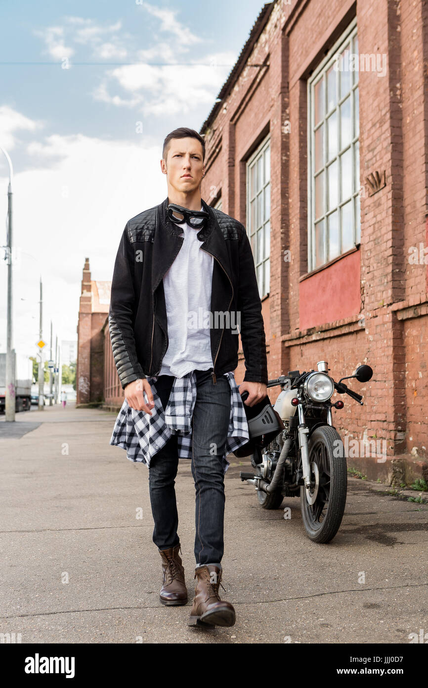Guapo rider biker en chaqueta de cuero negro, jeans y casco andando desde el clásico estilo racer moto. Moto custom made en vintage gar de stock - Alamy