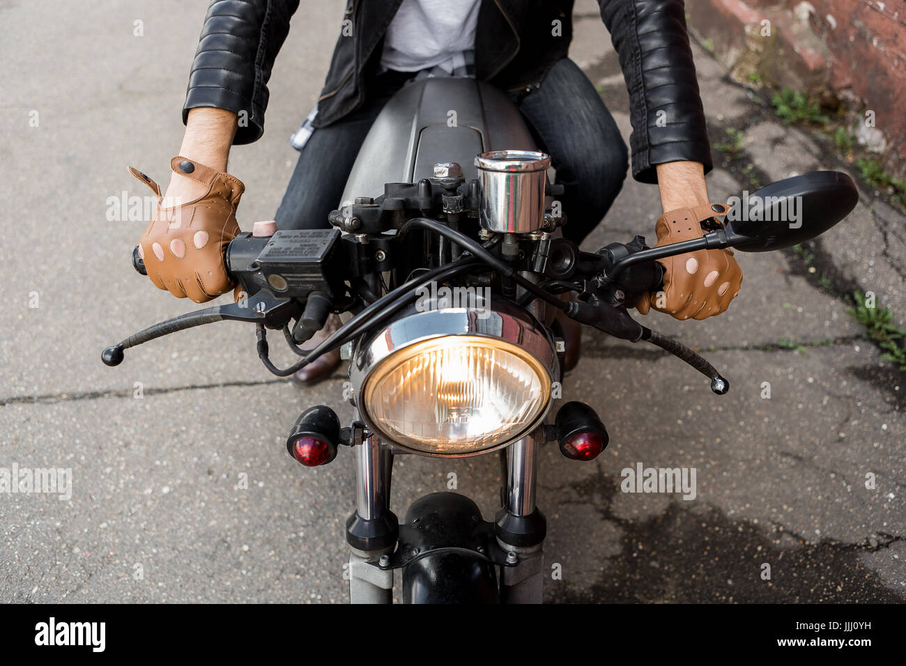 Primer plano de un hipster biker chico mano en guante piel mantenga el  control del acelerador de estilo clásico cafe racer moto. Moto custom made  en vintage garaje Fotografía de stock -