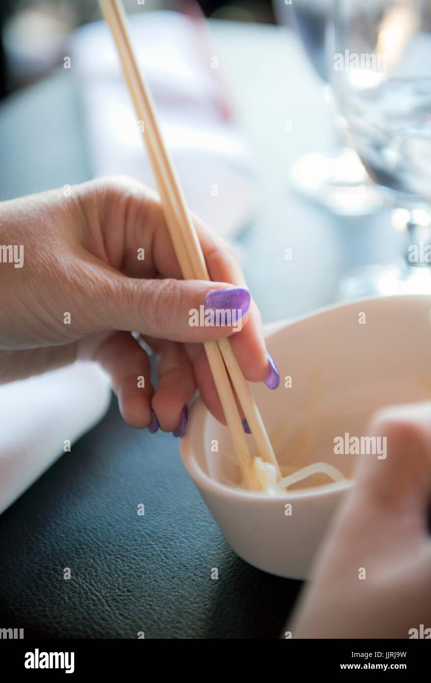 Las manos de una mujer con palillos y un tazón de comida asiática Foto de stock