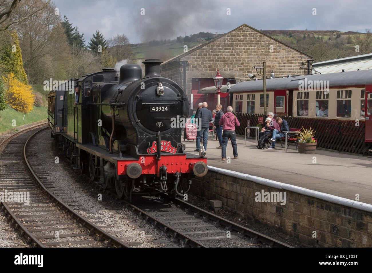 La gente mira una locomotora a vapor BR (ferrocarril Midland) 4F 0-6-0 43924 tirando hacia la estación, resoplando humo - Keighley & Worth Valley Railway, Inglaterra, Reino Unido. Foto de stock