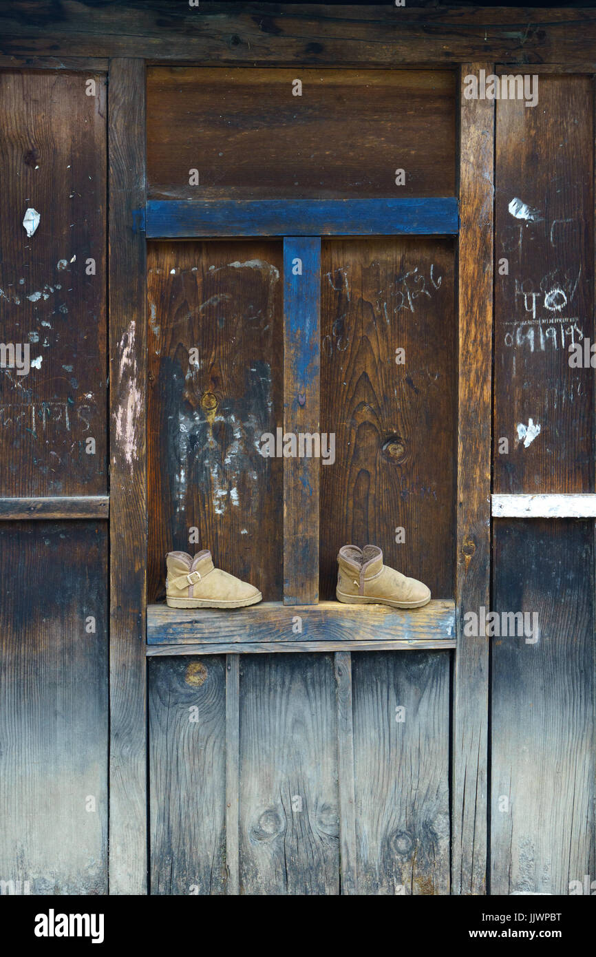 Par de botas a la izquierda en la estructura de los paneles de la pared exterior de una casa de madera en Nepal. Foto de stock