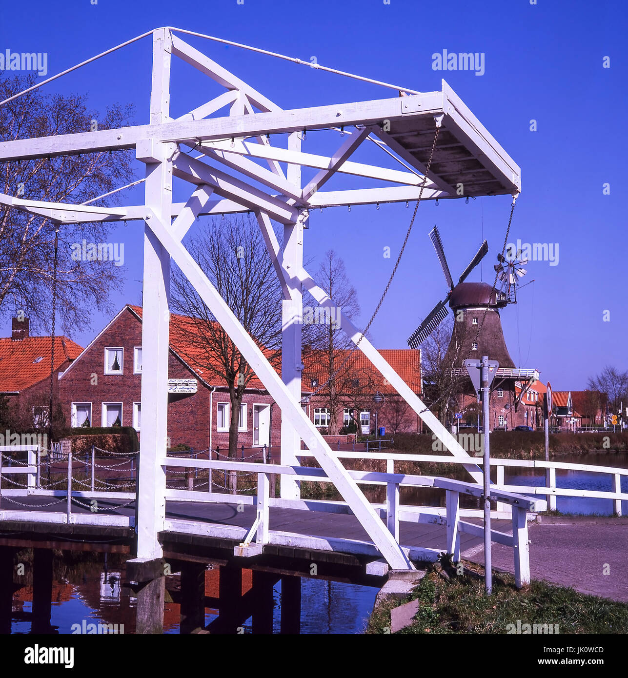 El "balance de blancos el puente sobre el canal de mittegrossefehn, en el fondo reetgedeckte windmill. plegable blanco puente sobre el canal en mittegrossefeh Foto de stock