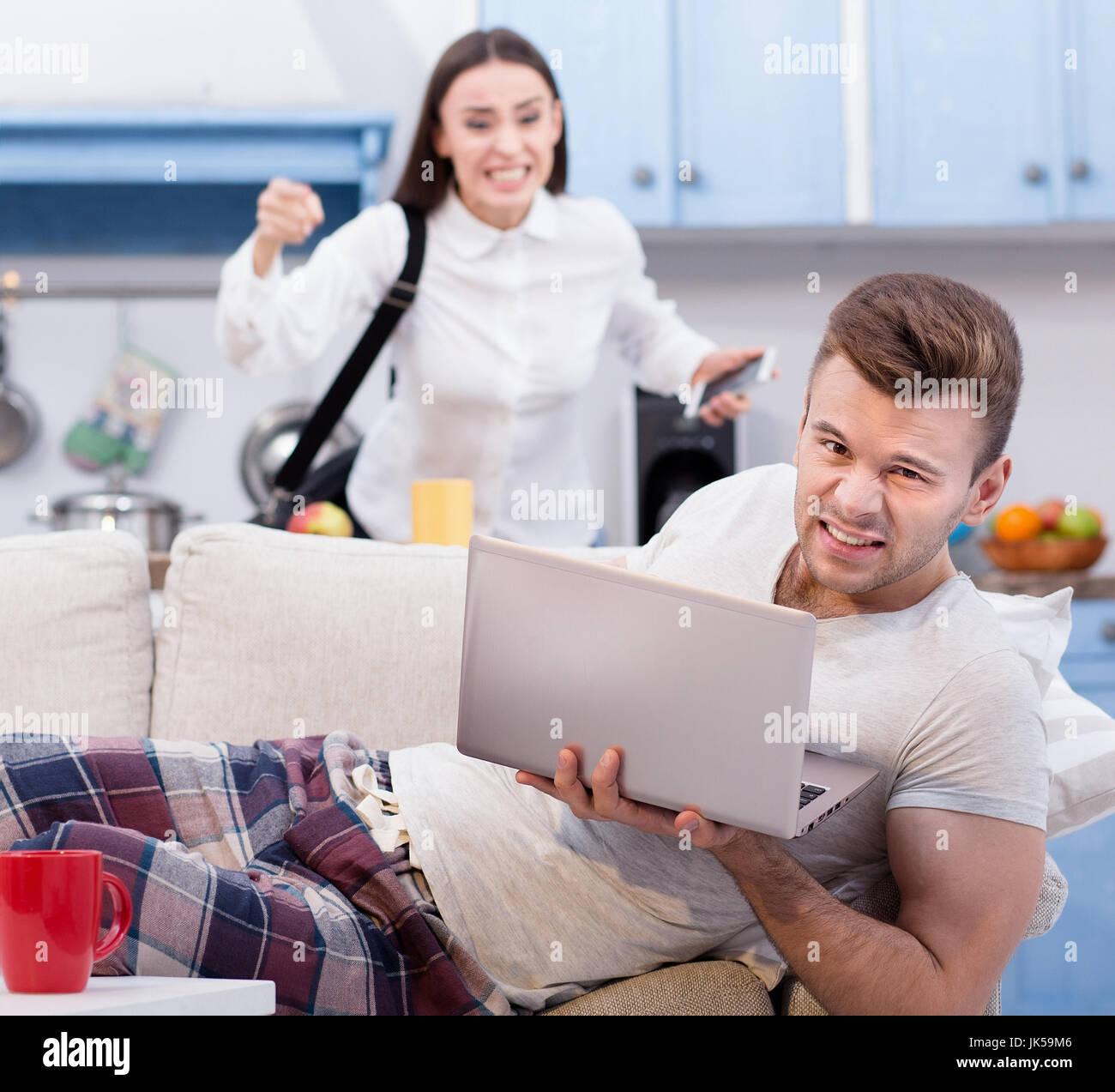 Perezoso marido en el sofá y su esposa furiosa, que va a trabajar. Foto de stock