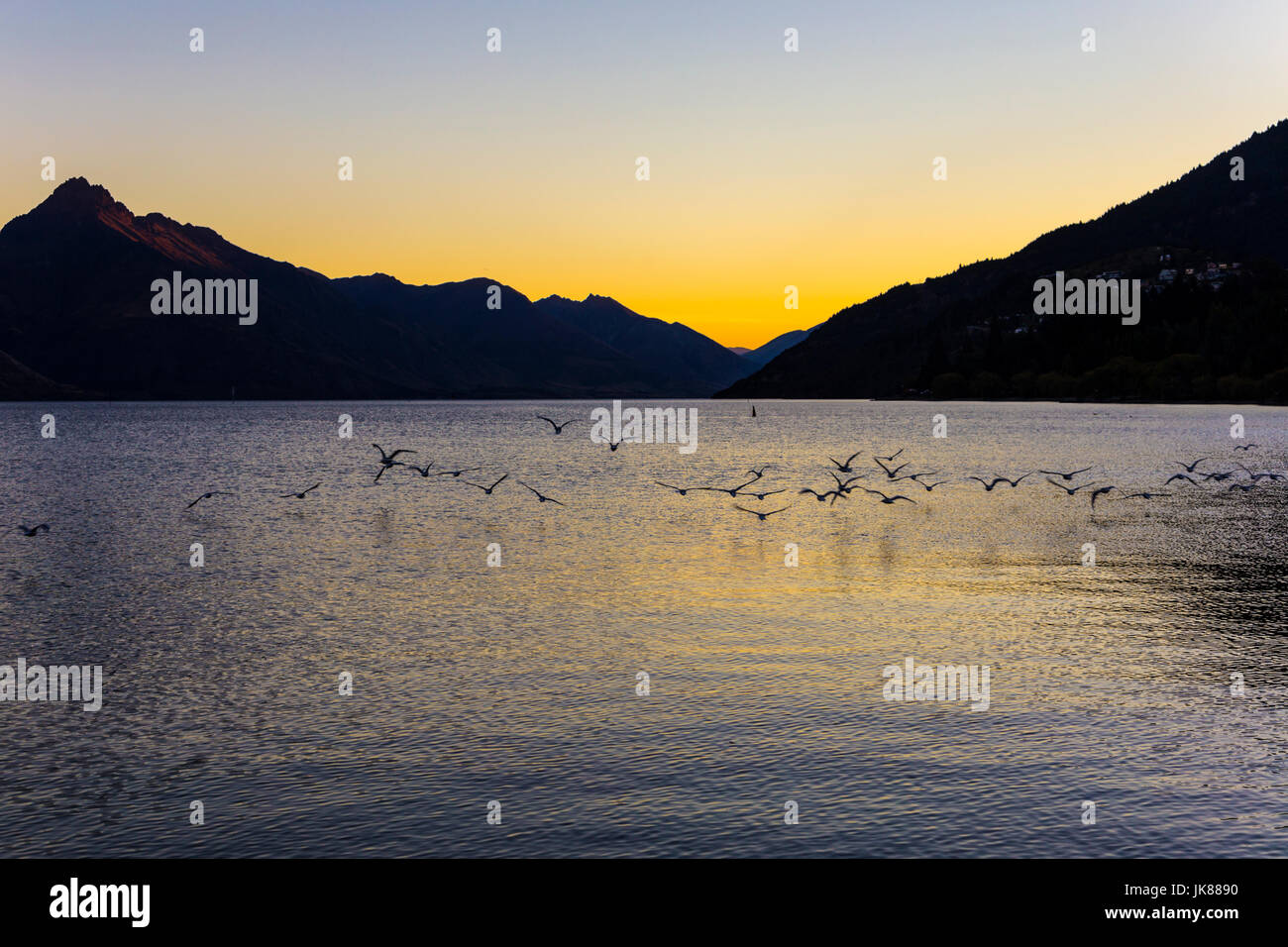 Las siluetas de las montañas y los pájaros volando sobre un lago al atardecer, (Lago Wakatipu, Queenstown, Isla del Sur, Nueva Zelanda) Foto de stock