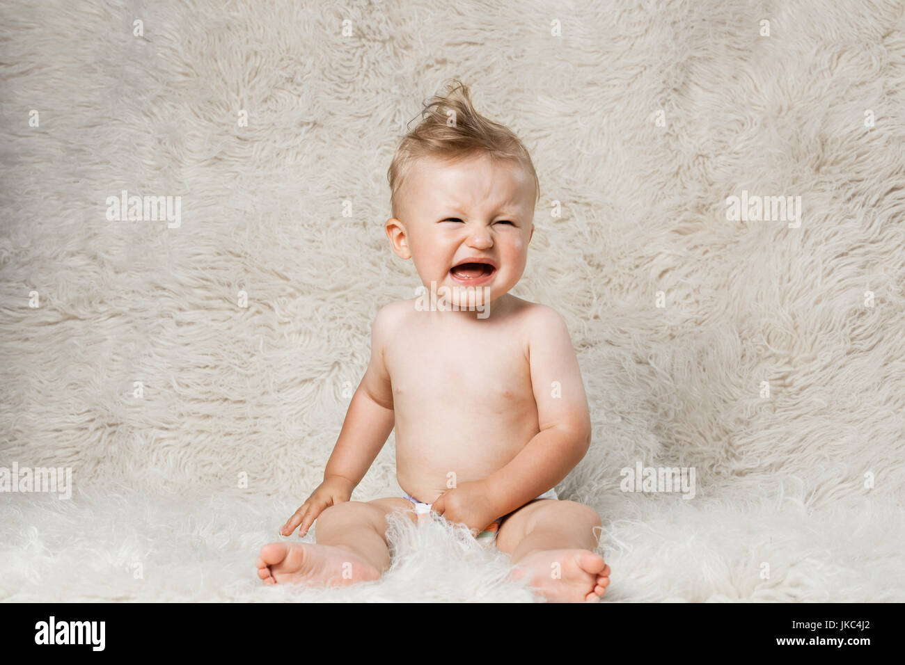 El llanto del bebé niño en pañales, sentada sobre una manta de lana shaggy caseros Foto de stock