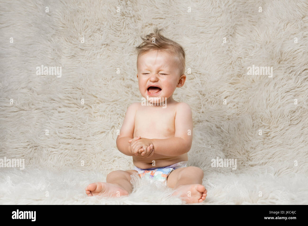 El llanto del bebé niño en pañales, sentada sobre una manta de lana shaggy caseros Foto de stock
