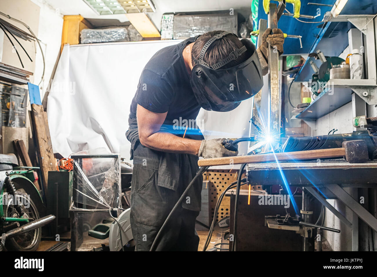 Hombre Fuerte soldador en ropa de trabajo trabajo duro y soldaduras con una  máquina de soldadura en la tela metálica Fotografía de stock - Alamy