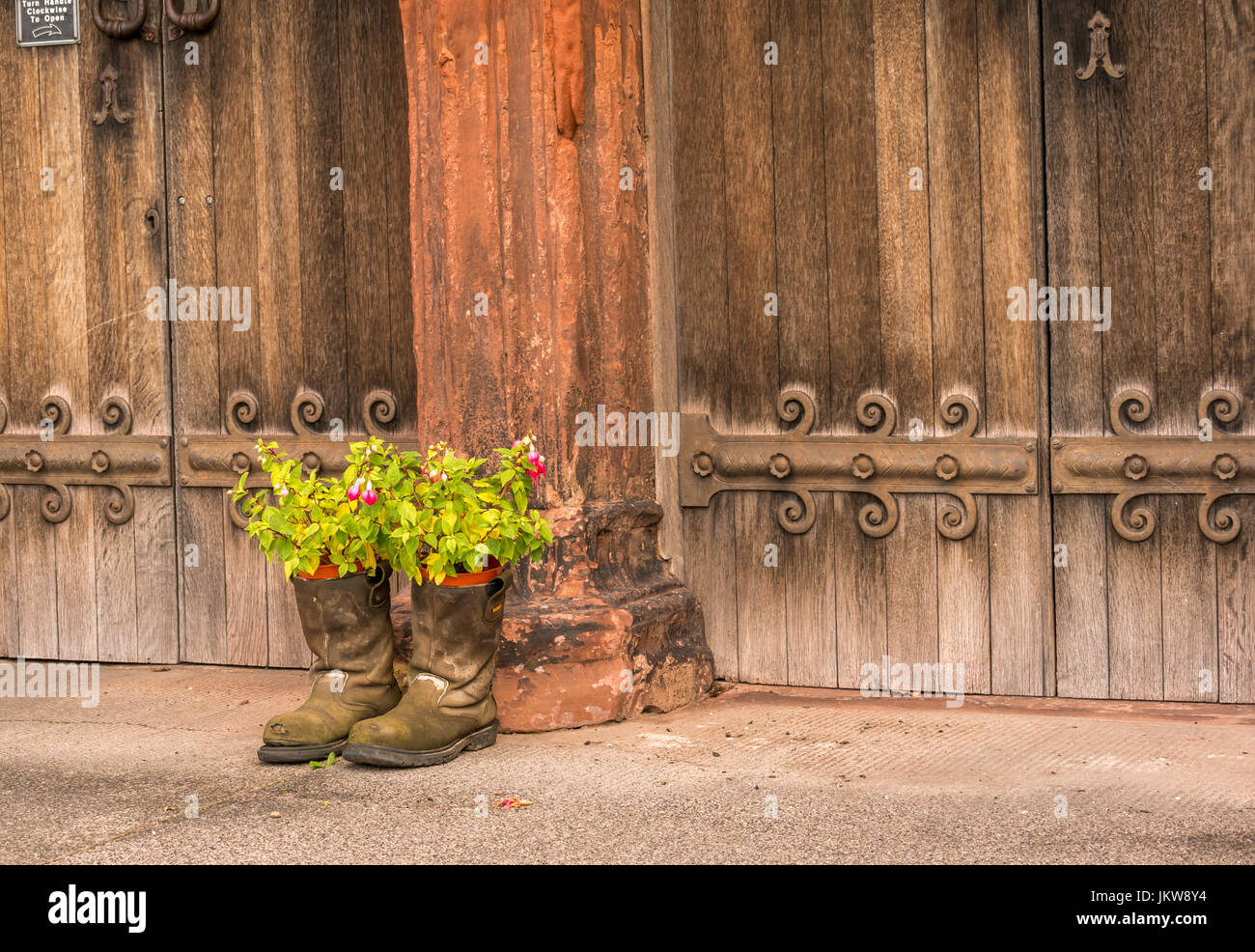 Los hombres botas viejas utilizada como maceta inusuales contenedores fuera antiguo de madera, las puertas de la iglesia St Mary's Church, Haddington, East Lothian, Escocia, Reino Unido Foto de stock