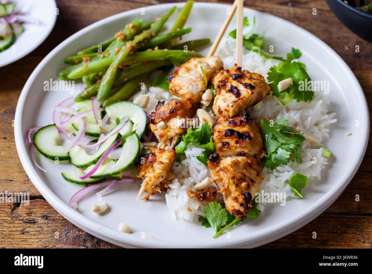 Brochetas de pollo Satay con arroz, ensalada de pepino y judías verdes Foto de stock