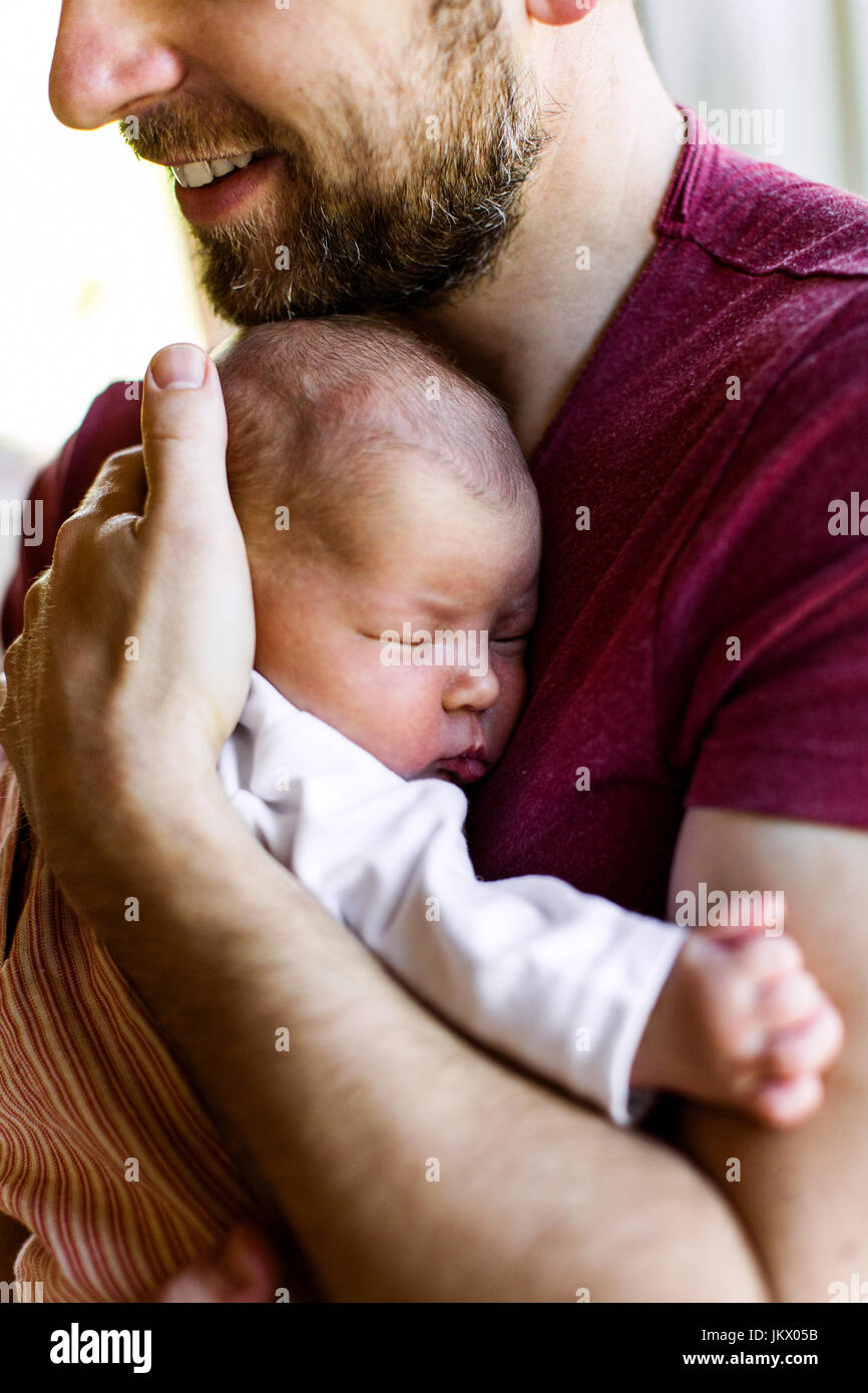 Padre joven irreconocible en casa sosteniendo a su bebé recién nacido gir Foto de stock