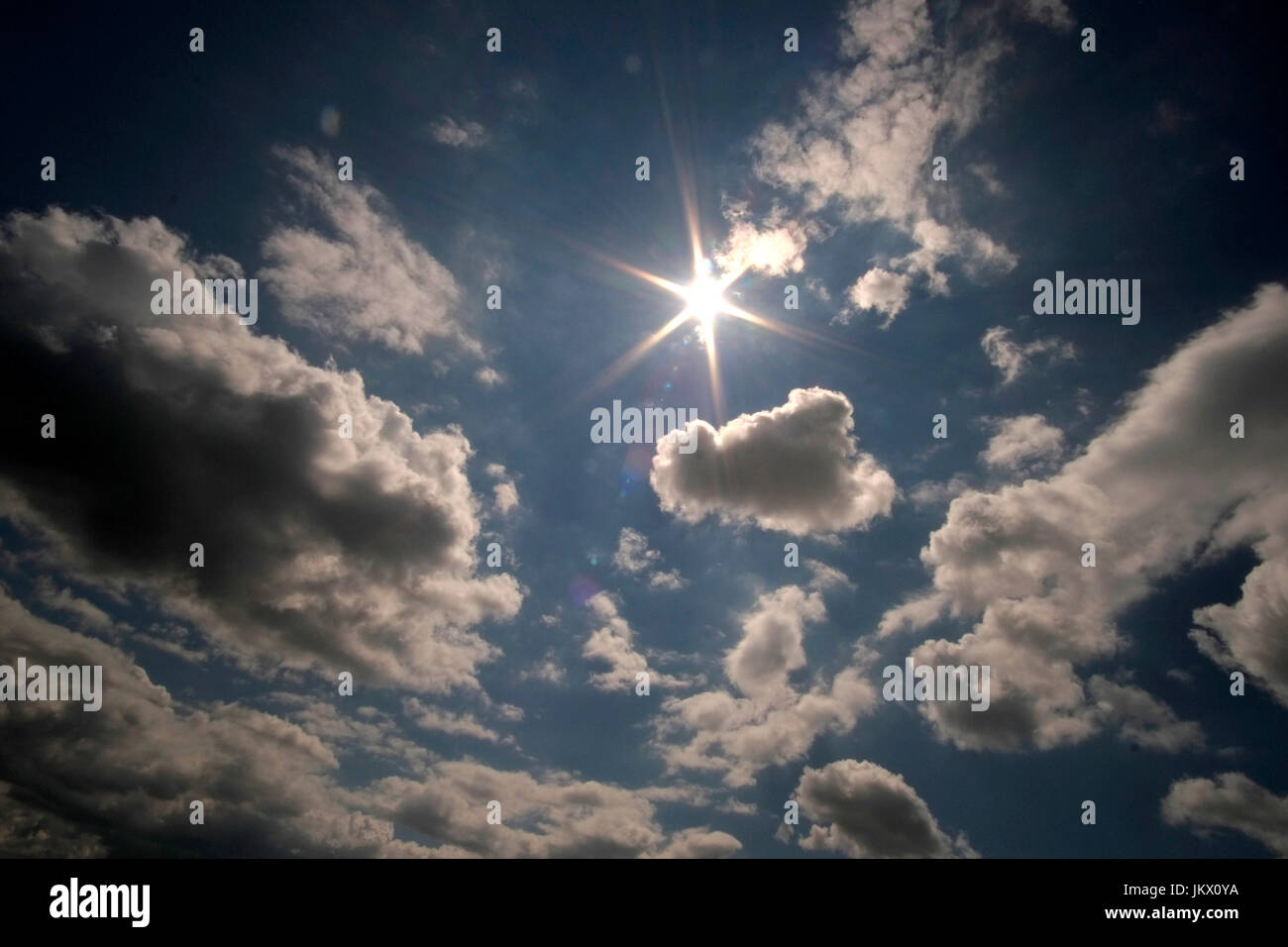 Un cielo azul con nubes blancas y un sol destello. Foto de stock