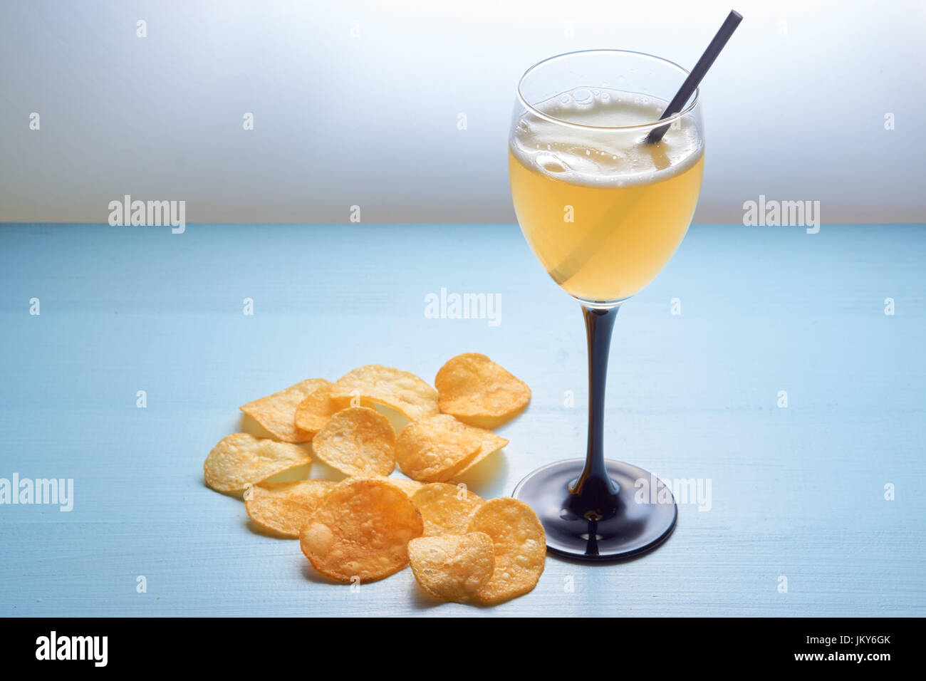 Vaso de cerveza ale dorada agitar mezcla de bebidas con paja potable. Queso patatas fritas aparte. amarillo sobre fondo azul de cerveza ordenadas el contraste de color Foto de stock