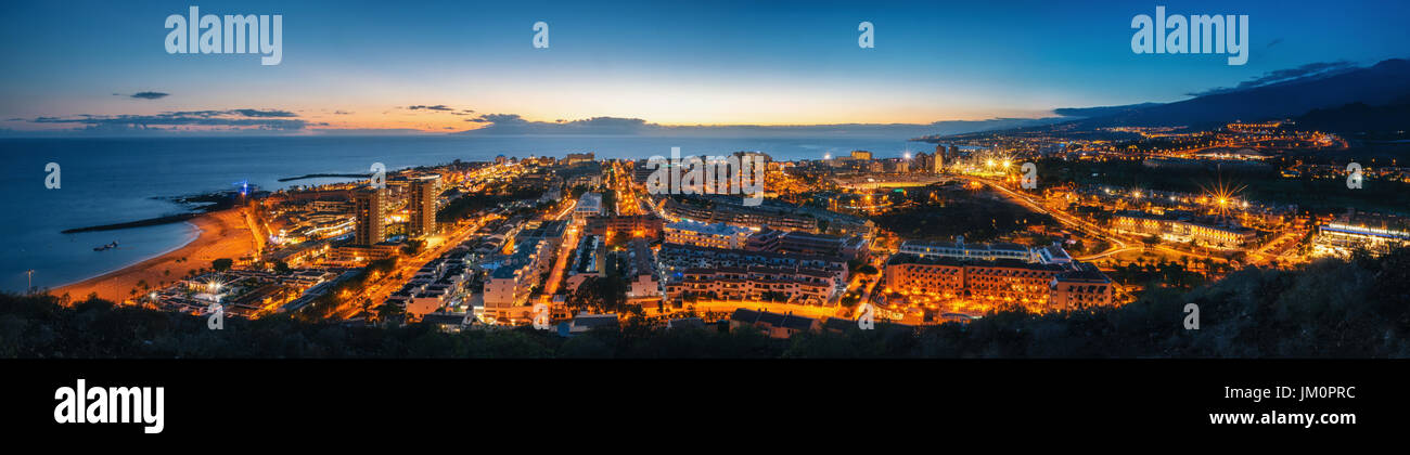 Vista panorámica del iluminado en la noche de las Américas contra el colorido atardecer cielo con luces en el horizonte de la isla de Tenerife, España Foto de stock