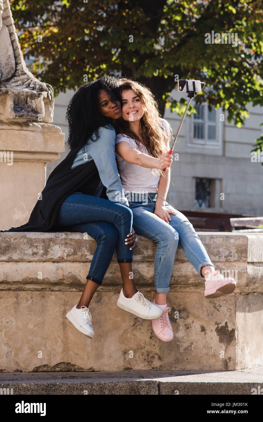 Dos jóvenes mujeres hermosas haciendo selfie abd cerca del monumento en el  centro de la ciudad. Las mujeres vestidas con ropa casual. Una mujer es  negro Fotografía de stock - Alamy