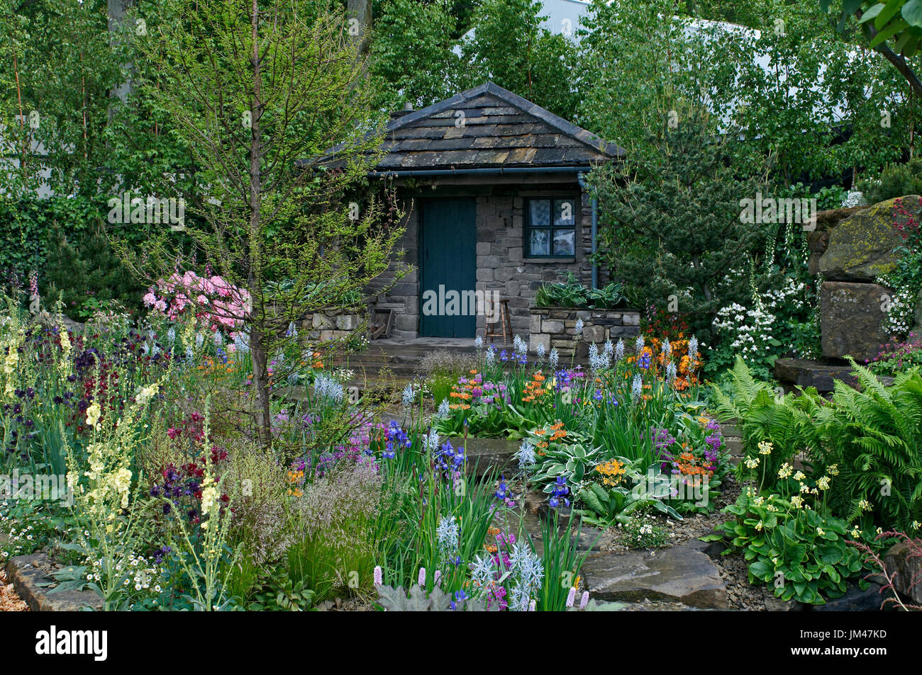 Un chalet y jardín situado en una arbolada rocalla con una colorida exhibición de flores Foto de stock