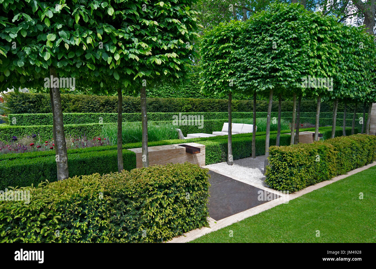 Un jardín clásico con una avenida de tejo carpe, box y conduce a una zona de agua y escultura Foto de stock