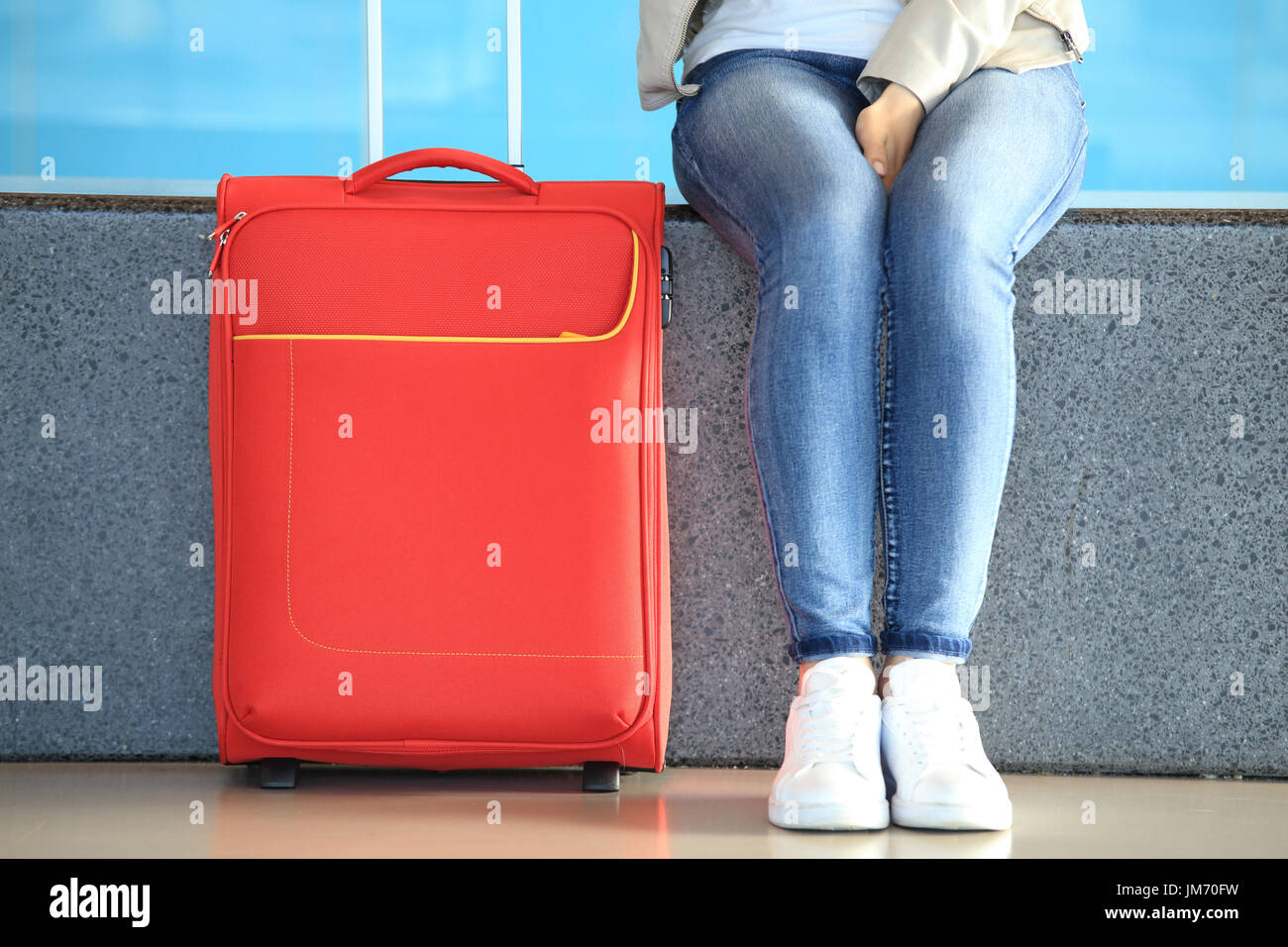Chica piernas en pantalones vaqueros cerca cerca la maleta roja. Antecedentes El tráfico de pasajeros Foto de stock