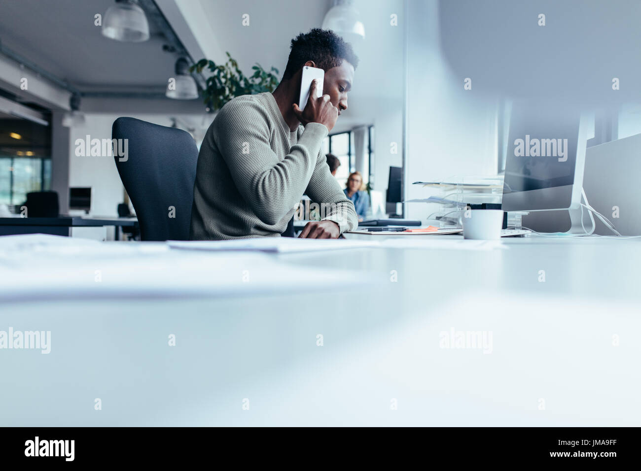 Hombre africano hablando por teléfono móvil. Empresario sentado en la oficina moderna con teléfono celular. Foto de stock