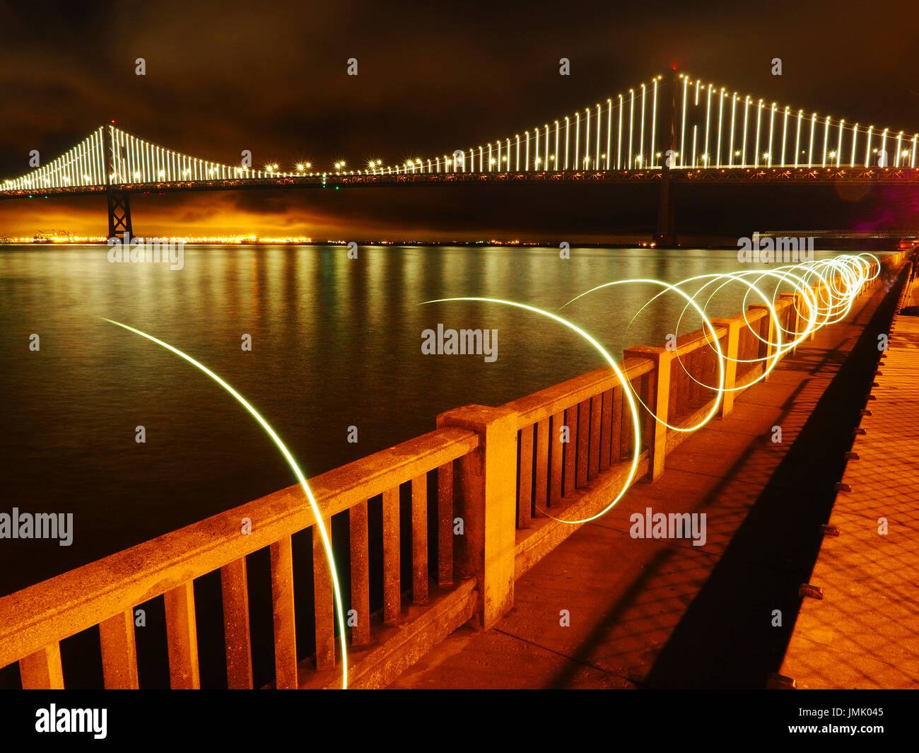 Puente de la Bahía de nuevo por la noche como se ve desde el embarcadero de San Francisco, California, con pintura de luz circular en primer plano Foto de stock
