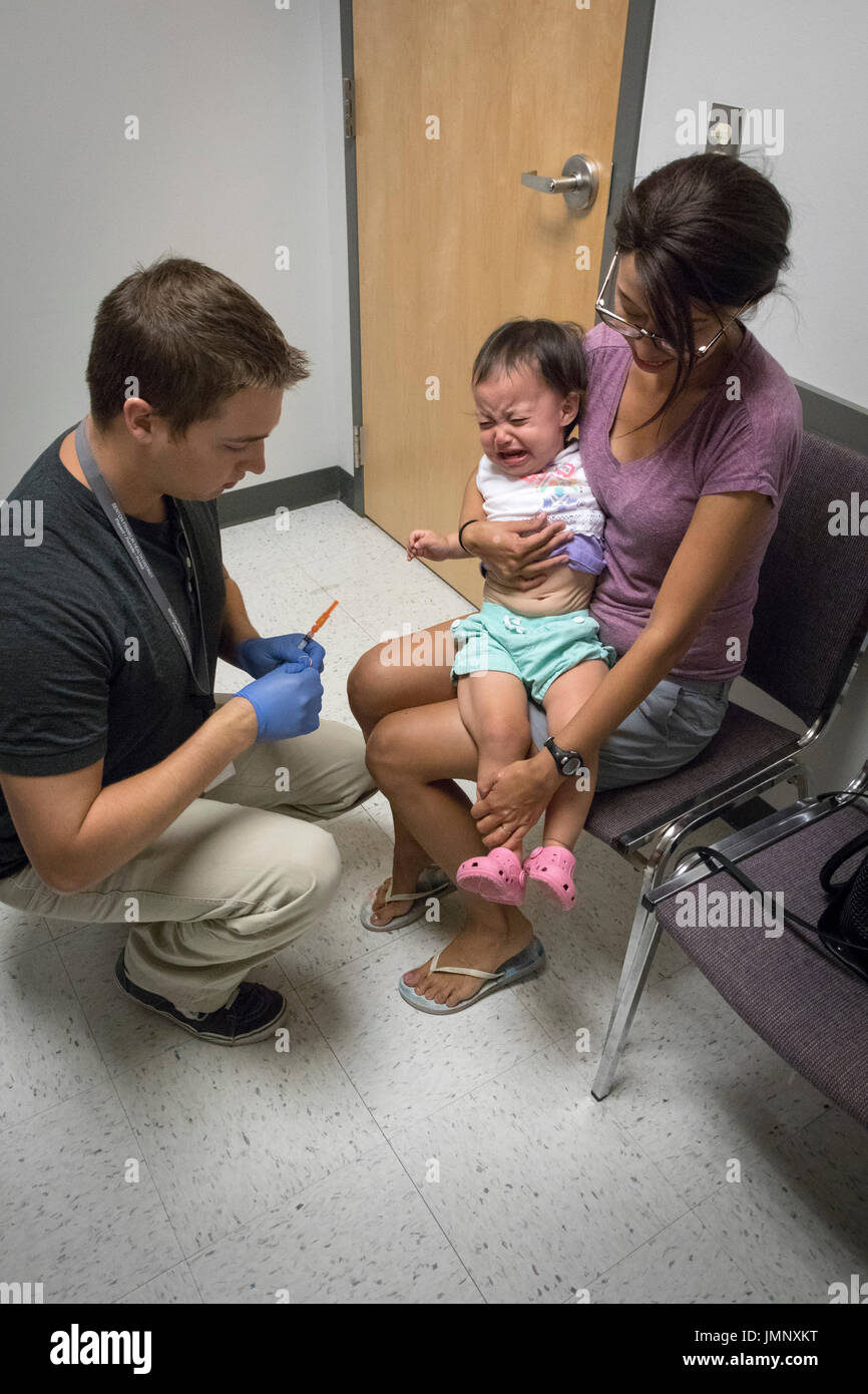 Bebé retenidos por la madre ansiosa recibir vacuna inyectable en el consultorio del médico Foto de stock