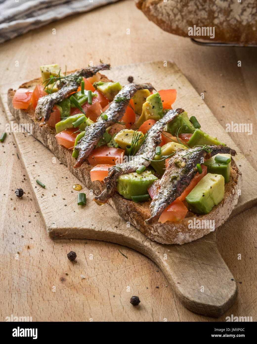 Pan agrio tostado con tomate, aguacate y anchoas. Foto de stock