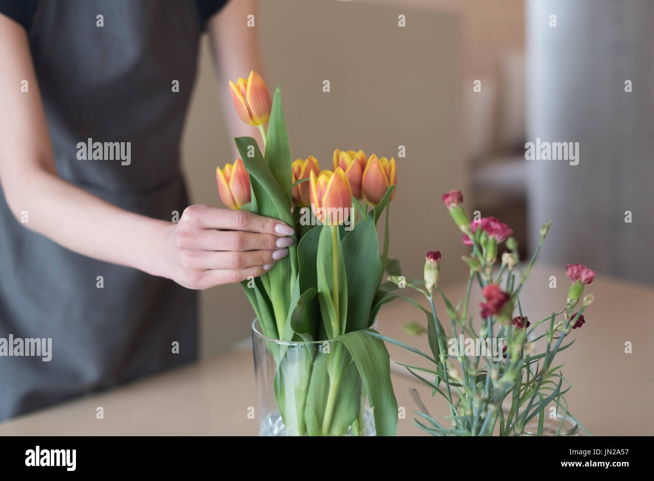 La sección central de la mujer organizando los tulipanes en un jarrón sobre la mesa del café Foto de stock