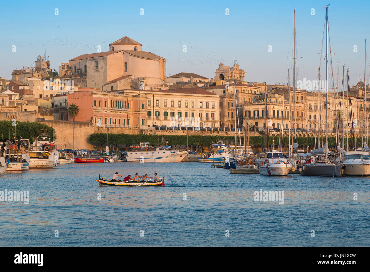Siracusa Sicilia paisaje urbano, vista de una tripulación de remo practicando en el puerto (Porto Grande) de Ortigia (Ortigia), Siracusa, Sicilia. Foto de stock