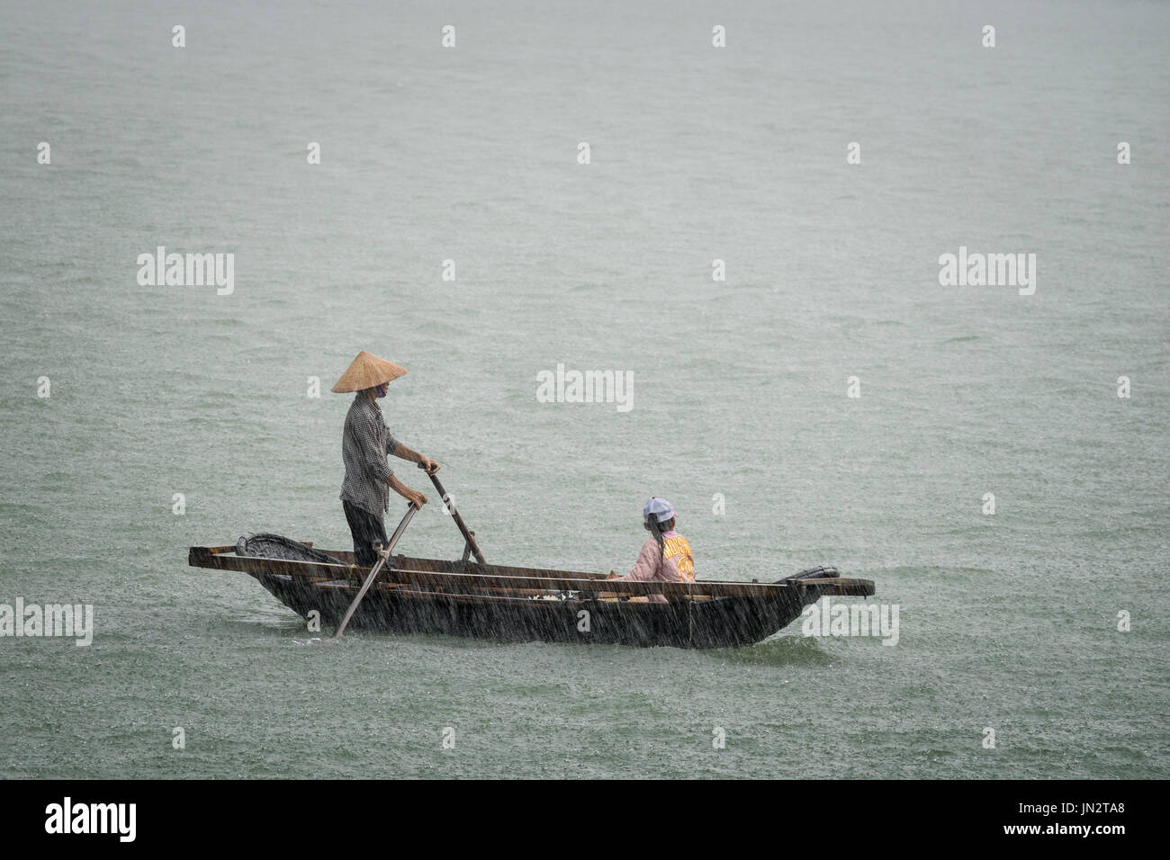 Padre e hija vietnamita en un bote de remos atrapados en la lluvia torrencial durante una tormenta en el mar Foto de stock