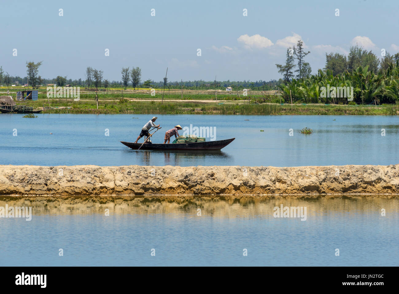 Mujer Vietnamita liberando larga red de pesca en el río Thu Bon mientras el hombre filas barco Foto de stock
