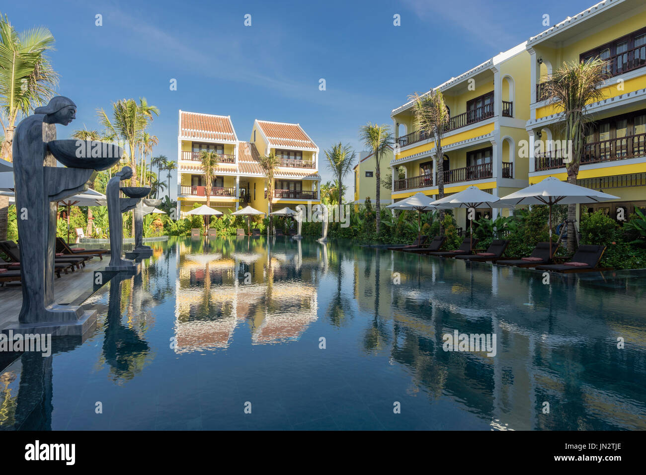 Las habitaciones del hotel alrededor de una piscina con estatuas y sombrillas en el precioso resort en Hoi An Vietnam Foto de stock