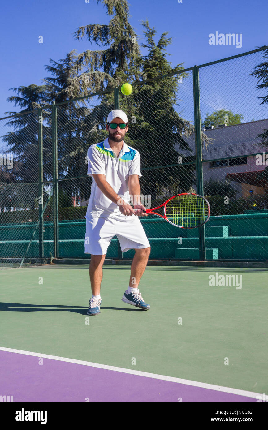 Tenista profesional jugando un partido de tenis en una cancha. Él está a punto de golpear la bola con la raqueta. La bola está suspendida en el aire. Foto de stock